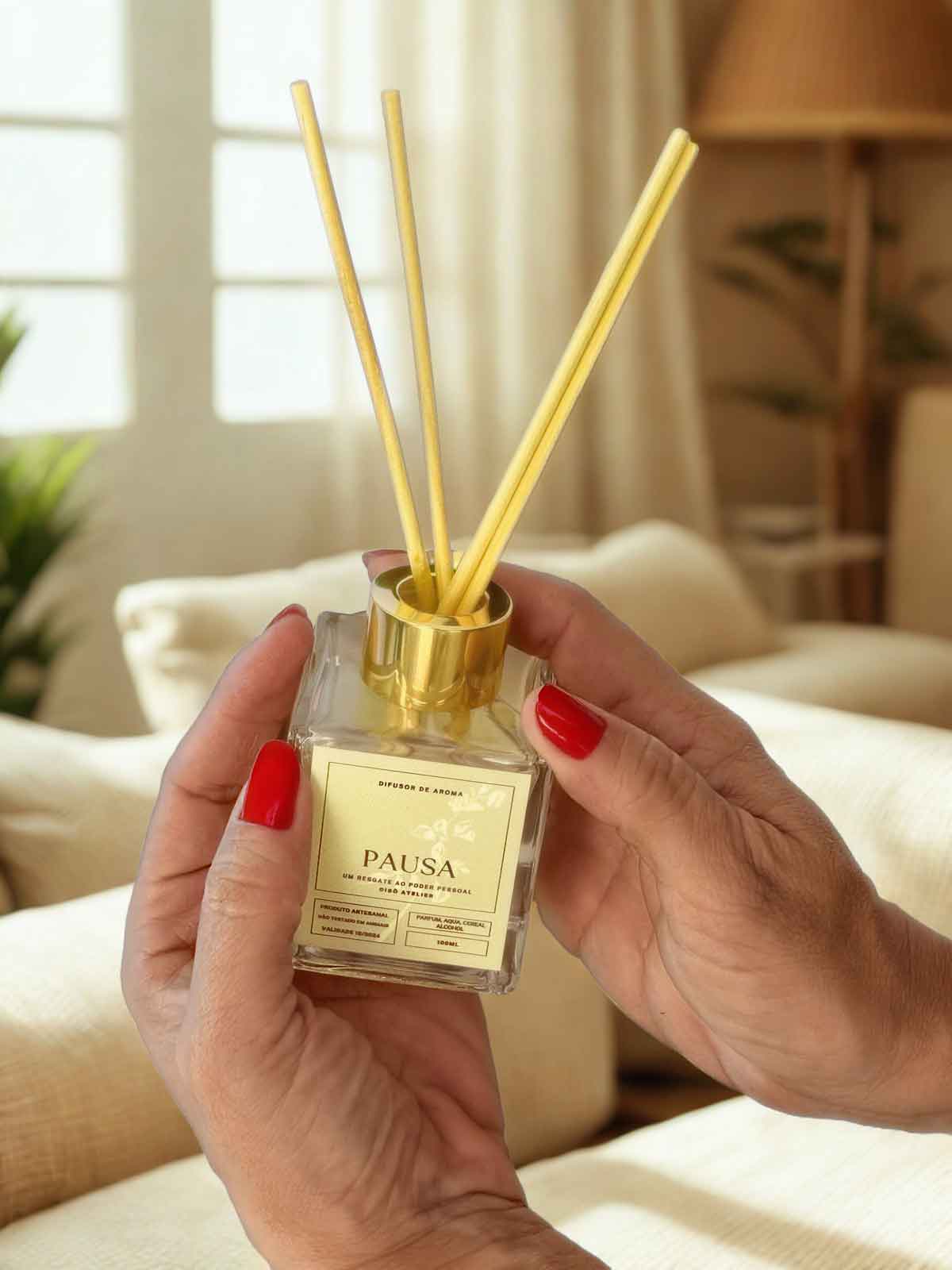 Difusor de ambientes Pausa 100ml Cisô Atelier em mãos, frasco de vidro com varetas e tampa dourada, ambiente aconchegante