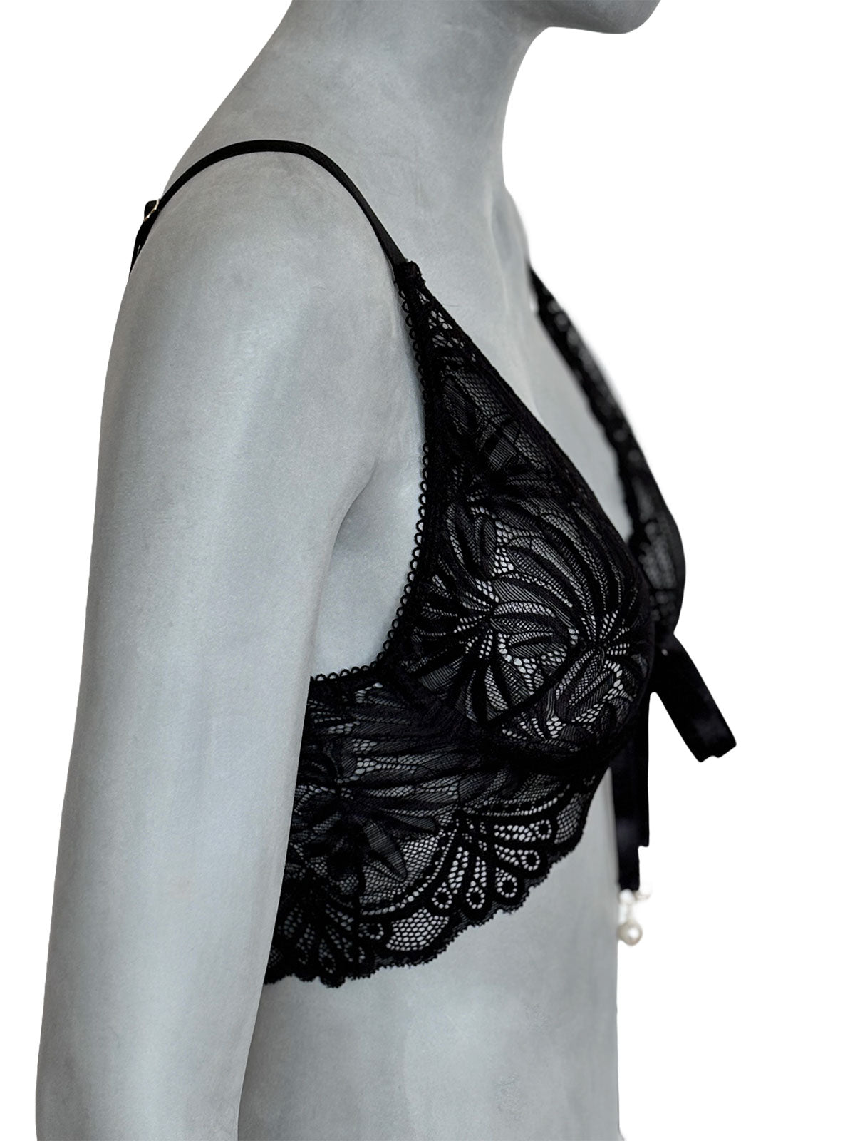 Sutiã Kamila preto em renda floral, decote profundo triangular com laço lateral e pingente de pérola, alça fina preta ajustável, vista lateral em manequim fundo neutro, lingerie sem bojo artesanal Cisô Atelier